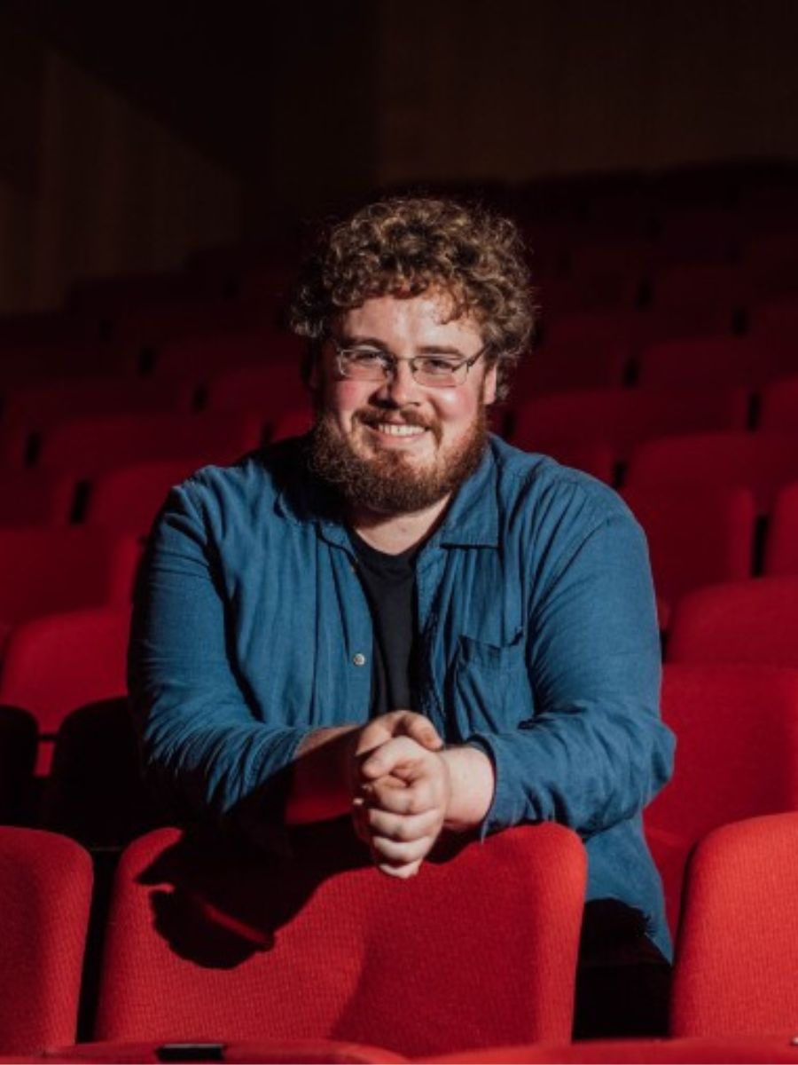 Colour image of Backstage Theatre Resident Artist Liam McCarthy sitting in an empty theatre