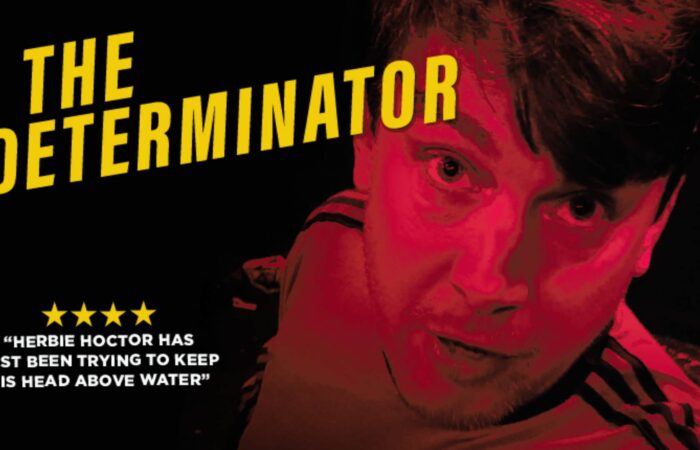 The Determinator - Charlie McGuinness bathed in red light against a black background