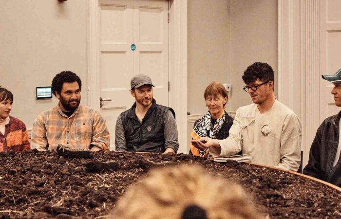 Distillation - Luke Casserly and audience members sitting around a table topped with peat.