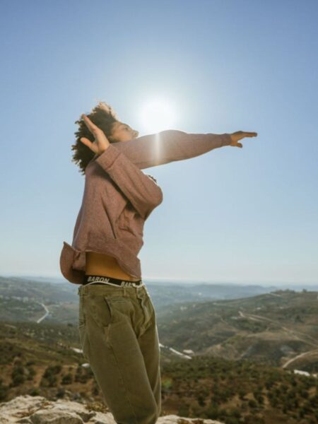 A male dancer performing on a hillside overlooking a tree-covered valley with the sun shining over his shoulder in Floating on a Dead Sea.