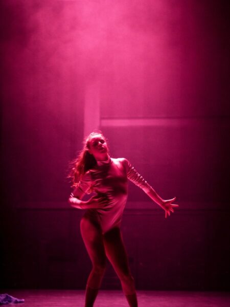 A young female dancer bathed in pink light strikes a pose during a performance of Night Dances