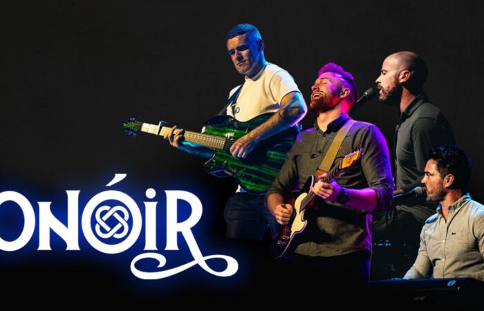 The members of Onóir in performance on a darkened stage. The name of the group appears on the lower left of the image.