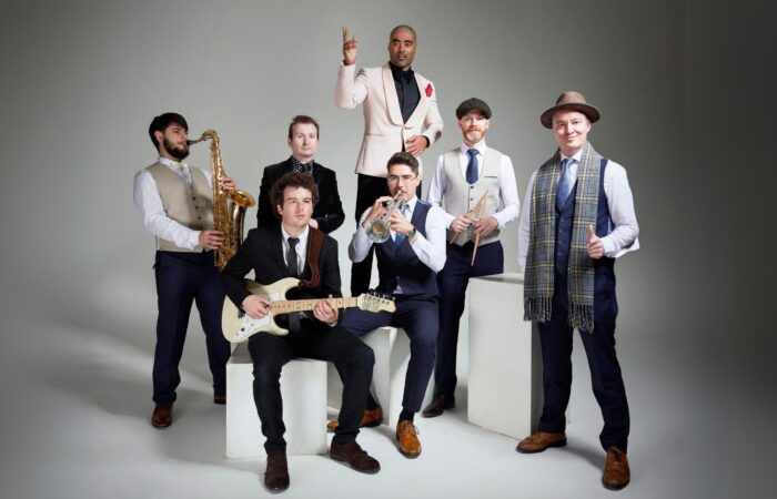 The Swing Cats posing with musical instruments against a grey background.