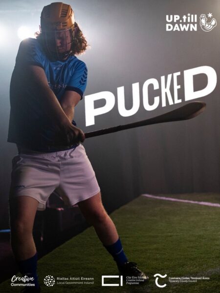 Action shot of a young man dressed in a hurling uniform and helmet as he strikes a sliotar. The word "Pucked" is overlaid atop the body of the hurley.