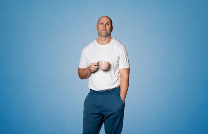Rory's Stories: Rory stands against a blue backdrop holding a pink mug with a perplexed look on his face.