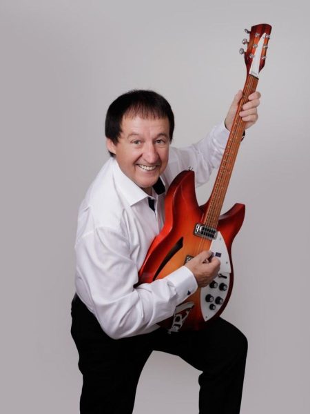 Declan Nerney - A smiling man in a white shirt and black trousers poses with a red electric guitar against a plain grey background.